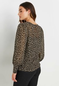 Blusa stampa leopardo realizzata in tessuto trasparente, con lunghe maniche a palloncino, apertura a oblò sul retro e dettagli arricciati in vita.