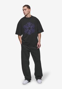Black oversized T-shirt with purple graphic design in the center, paired with loose-fitting, dark pants and white sneakers.