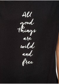 Zwarte mouwloze shirt met witte tekst die zegt: "Alle goede dingen zijn wild en vrij." Zacht katoenmateriaal met een relaxte pasvorm.