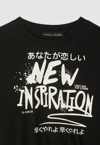 Czarna bawełniana koszulka z białym nadrukiem tekstowym, zawierająca napis „NEW INSPIRATION” oraz dodatkowy tekst w języku japońskim, ze wzorami przypominającymi rozpryski.