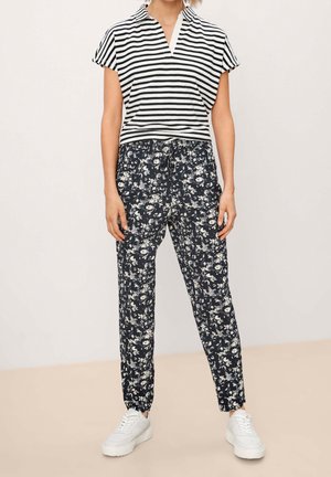 Gestreiftes schwarz-weißes Kurzarmshirt mit V-Ausschnitt, kombiniert mit marineblauen Hosen mit Blumenmuster und weißen Turnschuhen für einen lässigen Look.