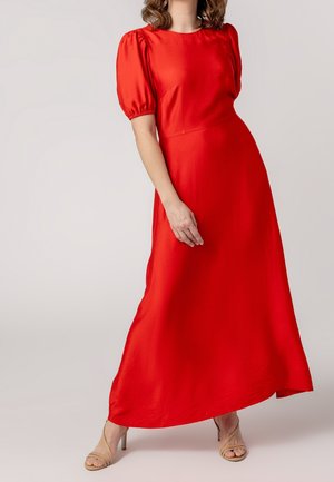 Rotes Maxikleid aus Satin mit rundem Ausschnitt, Puffärmeln und asymmetrischem Saum. Kombiniert mit nudefarbenen Riemchenabsätzen. Glatte Textur.