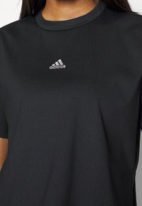 Svart ribbad t-shirt med korta ärmar, med rund halsringning och en liten silverfärgad Adidas-logga på bröstet.