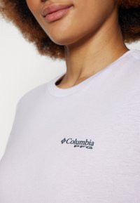Svijetlopurple majica od pamuka sa okruglim izrezom i kratkim rukavima, sa crnim Columbia PFG logotipom na prsima. Glatka tekstura.