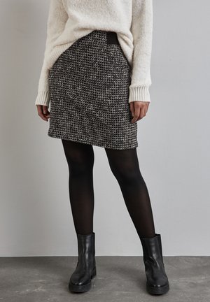 Jupe en tweed noir et blanc avec une forme cintrée, une surface texturée et une taille élastique. Associée à des collants noirs et des bottines.
