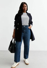 Granatowy dwurzędowy płaszcz na białej i granatowo paskowanej koszulce, wysokie niebieskie dżinsy i białe trampki z brązowymi podeszwami. Czarna torebka.