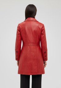 Red leather coat with a tailored fit, featuring a belted waist, long sleeves with button accents, and a smooth finish.