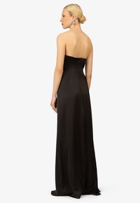 Schwarzes trägerloses Abendkleid aus Satin; taillierter Oberteil mit einem glatten, fließenden Rock. Der Rücken enthält einen verdeckten Reißverschluss und eine Schlitzeinfassung.
