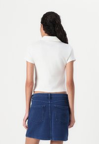 Vit polotröja med korta ärmar, krage, kombinerad med en blå denim minikjol med bakfickor och midjeband.