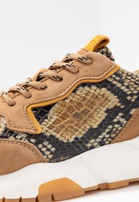 Baskets en suédine beige et matériau synthétique à motifs dans des nuances de marron et jaune, avec une semelle blanche épaisse et des détails en lacets.