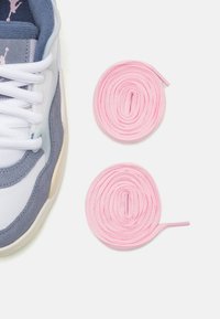 Tenis ar baltu un pelēku zamšādu, ar gaiši ziliem akcentiem un rozā apļu šņorēm blakus uz vienkārša fona.