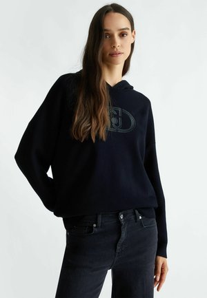Felpa nera oversize con stampa del logo sul davanti, realizzata in tessuto morbido. Abbinata a jeans neri con una vestibilità slim e design a cinque tasche classico.
