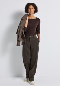 Brun långärmad topp kombinerad med högmidjade, texturerade mörkbruna byxor med diagonala ränder och framknäppning.