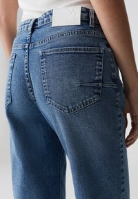 Jeans in denim di blu medio con una trama sbiadita, dotati di due tasche posteriori e di un'etichetta bianca in vita.