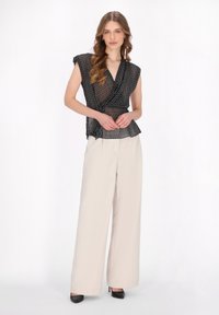 Zwart gebloemd wikkelshirt met korte mouwen, gecombineerd met hoog-getailleerde beige wijde broek en zwarte hakken. Soepele stof, moderne silhoeet.