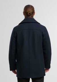 Navy Wollmantel mit strukturiertem Kragen, langen Ärmeln und geradem Schnitt. Glatte Textur mit minimalen Nähten auf der Rückseite.