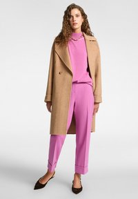 Camelkleurige wollen jas, roze gebreide trui, roze broek en bruine puntige flats. Opmerkelijke details: dubbelbreasted sluiting en omgeslagen broekspijpen.