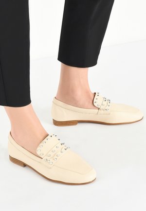 Roomkleurige leren loafers met metalen studs op de wreef, een platte houten hak en een gestroomlijnd ontwerp met een puntige neus.