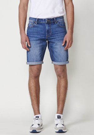 Shorts de mezclilla en azul claro con un acabado desgastado, con puños enrollados, cinco bolsillos y detalles de costura en contraste.