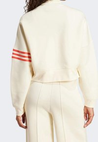 Kortad krämfärgad sweatshirt med röda randiga detaljer på ärmarna, med en avslappnad passform och mjuk textur, matchad med krämfärgade byxor.