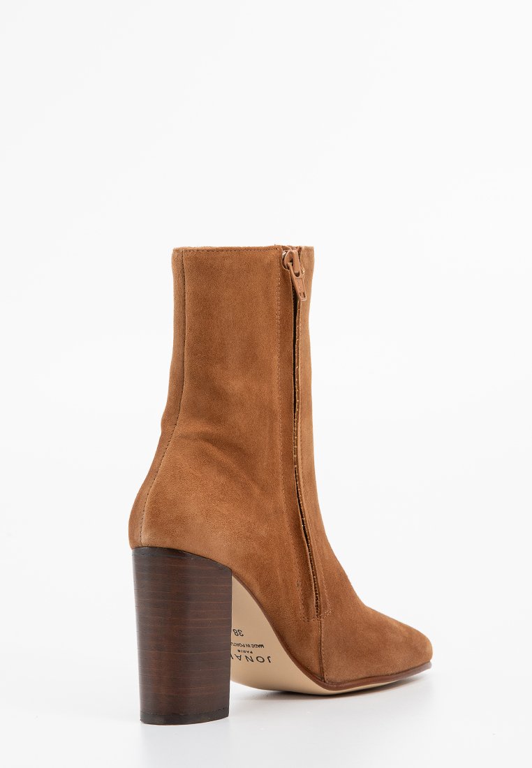 Bottine en cuir suédé marron avec un bout rond, une fermeture éclair sur le côté et un talon en bois. Texture lisse et silhouette ajustée.