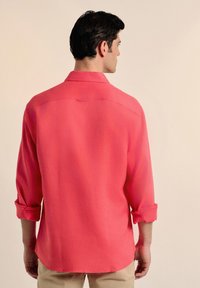 Camisa de botón color coral con cuello y mangas enrolladas. La tela ligera y el corte relajado acentúan el diseño casual.