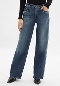 Weite Jeans aus dunkelblauem Denim, ausgestattet mit dekorativen Nieten entlang der vorderen Taschen und Seitennaht, mit einer glatten, strukturierten Oberfläche.