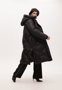 Černá péřová bunda s kapucí, se vzorem diamantu, s patentkami a podšívkou v leopardím vzoru. Vytvořena s černými kalhotami a botami.