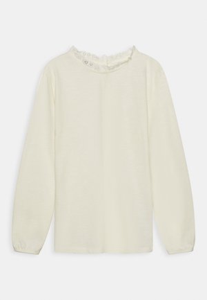 Top de manga larga en color crema con borde de encaje con forma de concha alrededor del escote redondo y puños elásticos.