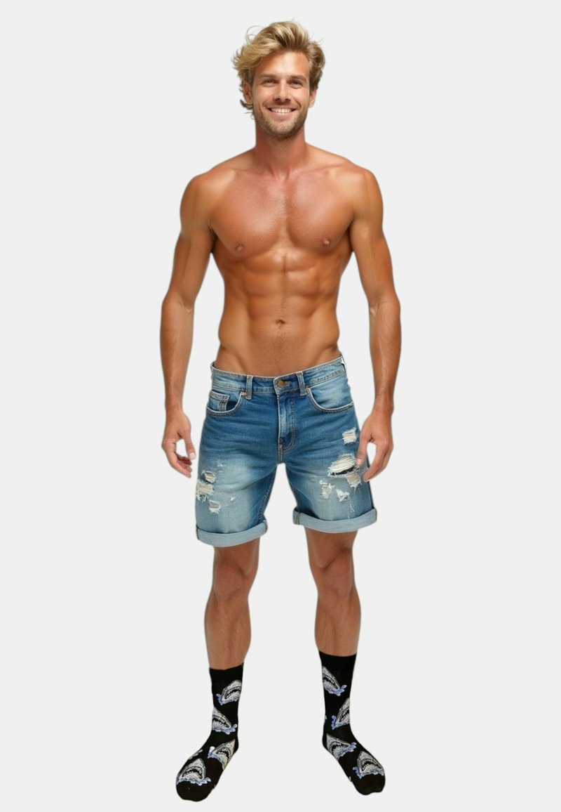 Denimshorts, lyseblå med slidte detaljer, opkrøllede kanter; båret med sorte sokker med hvide hajgrafikker. Lys hud, muskuløs bygning.