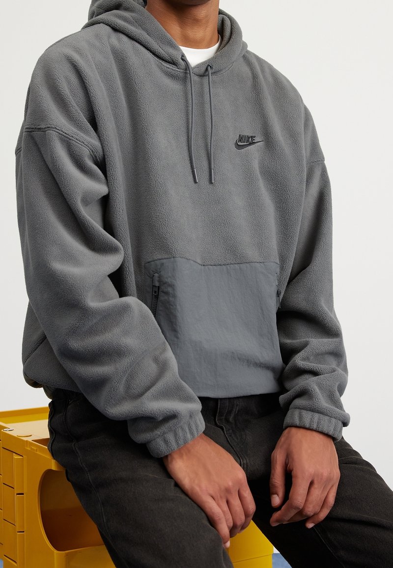 Šedá mikina z fleecu s klokankou a černým zipem. Obsahuje kapuci se stahovací šňůrkou a vyšívané logo na hrudi.