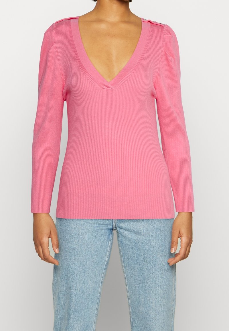 Różowy prążkowany top z długim rękawem, głębokim dekoltem w szpic i usztywnianymi ramionami, ozdobiony guzikami na ramionach. Połączony z jasnoniebieskimi dżinsami.