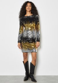 Vestido de lentejuelas brillante con mangas largas, que presenta un degradado de negro, dorado y plateado. Combinado con botas de vaquero negras. Textura suave.