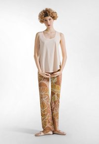 Jasnobeżowy top na ramiączkach w połączeniu z luźnymi, wzorzystymi spodniami w ziemistych odcieniach, ozdobionymi dużymi motywami liści oraz miękką fakturą.