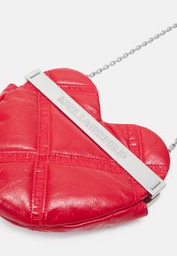 Borsa a forma di cuore in pelle rossa con logo in rilievo e tracolla in catena argentata, caratterizzata da motivi cuciti orizzontali e una chiusura metallica.