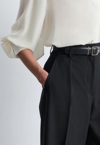 Black tailored trousers with a wide leg and side pockets, paired with a loose-fit cream blouse featuring wide, gathered sleeves.