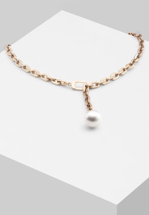 Collar de cadena de oro con un único colgante grande de perla blanca que cuelga de un eslabón de forma cuadrada sobre una superficie blanca.