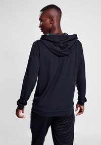 Zwarte hoodie met lange mouwen van textuurstof en een trekkoordkap, gedragen over bijpassende zwarte sportbroek. Achteraanzicht, met slank ontwerp.