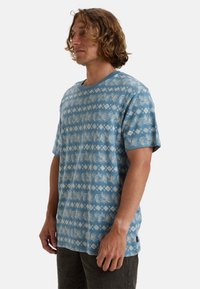 Short-sleeve shirt made of light blue fabric featuring a white leaf and diamond pattern with a round neck and relaxed fit.