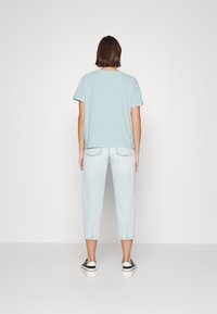 Maglietta azzurro chiaro di taglia comoda con maniche corte, abbinata a pantaloni cropped in denim chiaro e sneakers nere con suole bianche.