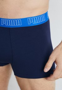 Dunkelblaue Boxershorts mit einem kontrastierenden blauen Bund, der das "PUMA"-Logo trägt. Weicher Stoff, figurbetonter Schnitt, ohne zusätzliche Muster.