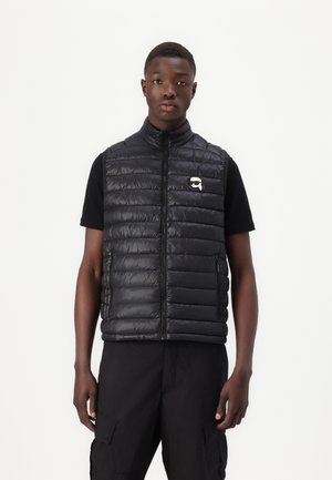 Black puffer vest with horizontal quilted design, front zipper, and side pockets. Features a small logo on the left chest.