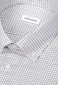 Chemise blanche à motif quadrillé gris, col boutonné, avec une étiquette portant la mention "seidensticker" à l'intérieur du col.