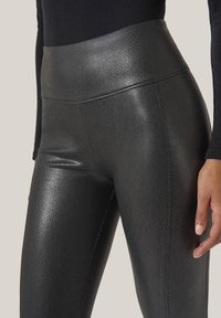 Svarta höga leggings i strukturmaterial, med ett subtilt mönster och slät yta. Närbilden framhäver form och passform.