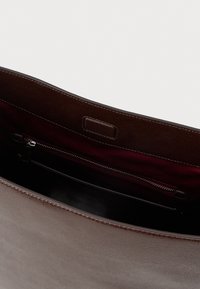 Bolsa de couro castanho com uma textura suave, apresentando um bolso com fecho e um rico forro bordeaux. Design de topo aberto sem acessórios externos.