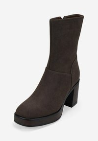Bota de ante marrón oscuro hasta la mitad de la pantorrilla con tacón grueso apilado y puntera redonda, que cuenta con un cierre de cremallera lateral.