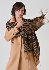 Braun und schwarz gemusterter Schal mit Tierdruck und Chevron-Details, mit fransigen Kanten, getragen über einem hellbraunen Mantel.