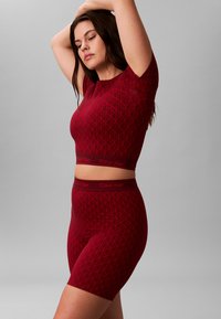 Rød mønstret tætsiddende top og shorts sæt med geometrisk design. Calvin Klein branding på taljebåndene. Glat tekstur, korte ærmer.