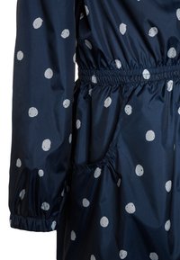 Marinblå regnkappa med vita cirkulära mönster, elastisk midja, långa ärmar och en sidficka. Slät, lätt material.