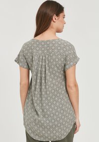Grønne mønstrede top med en fleksibel design, korte ærmer og en plissering detalje bagpå. Har cirkulære motiver over hele stoffet.